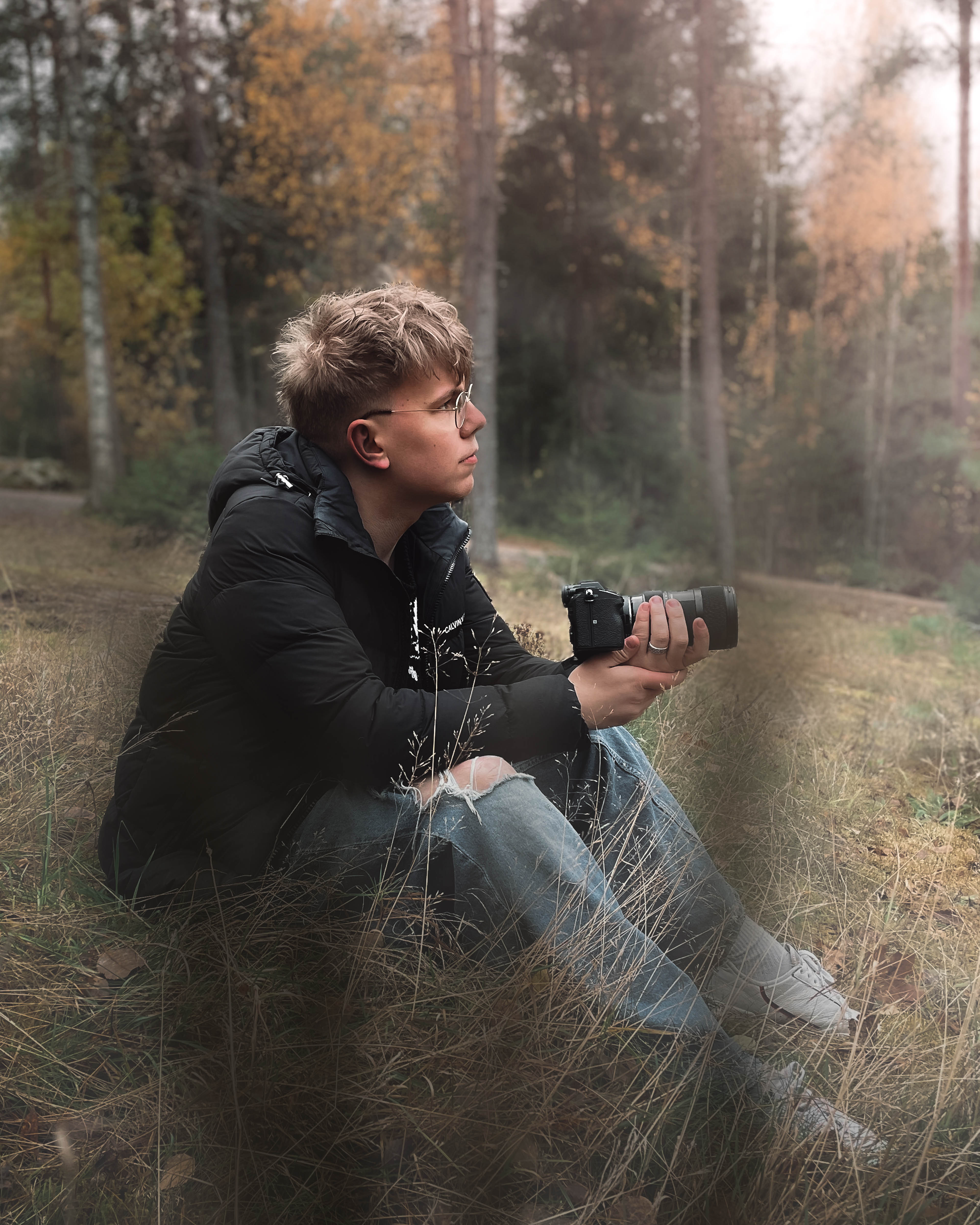 Valtti poseeraa metsässä istuen pois kamerasta kamera kädessään.